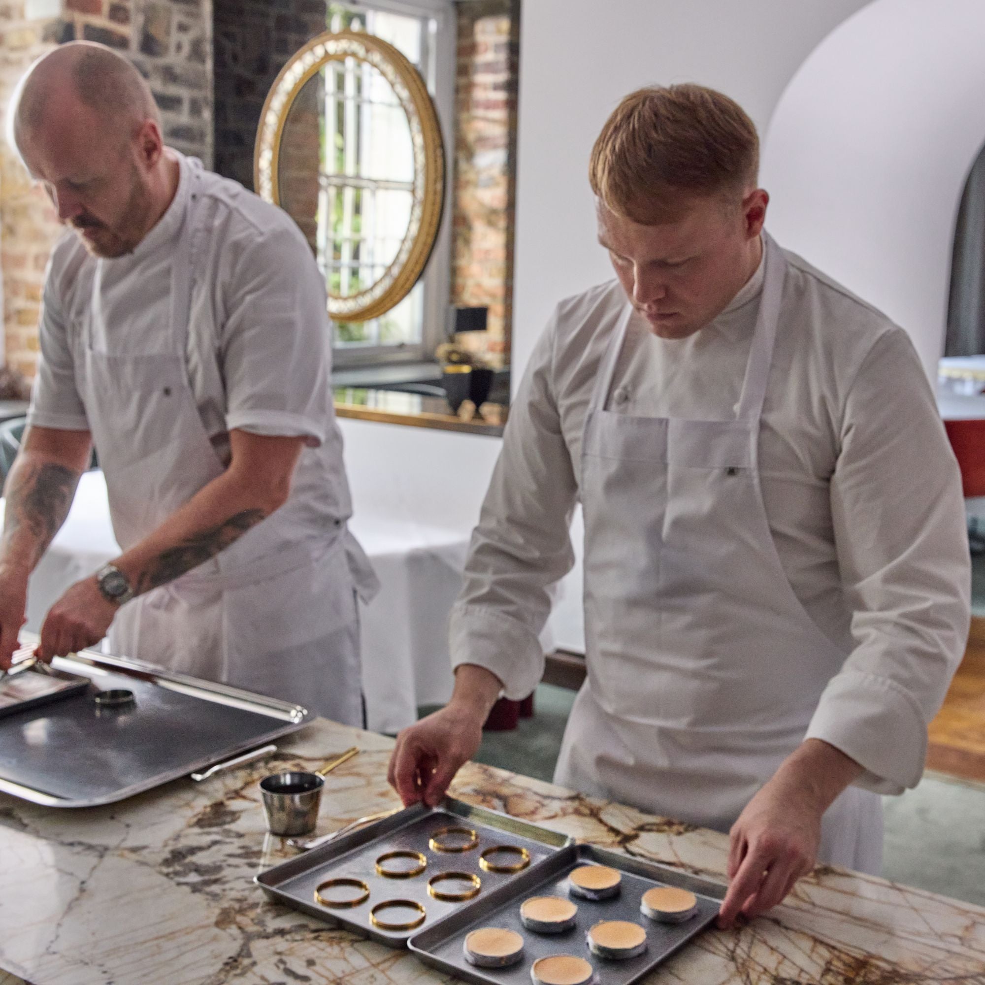 Two Chefs in the kitchen preparing dishes using stackable ring moulds placed on trays.