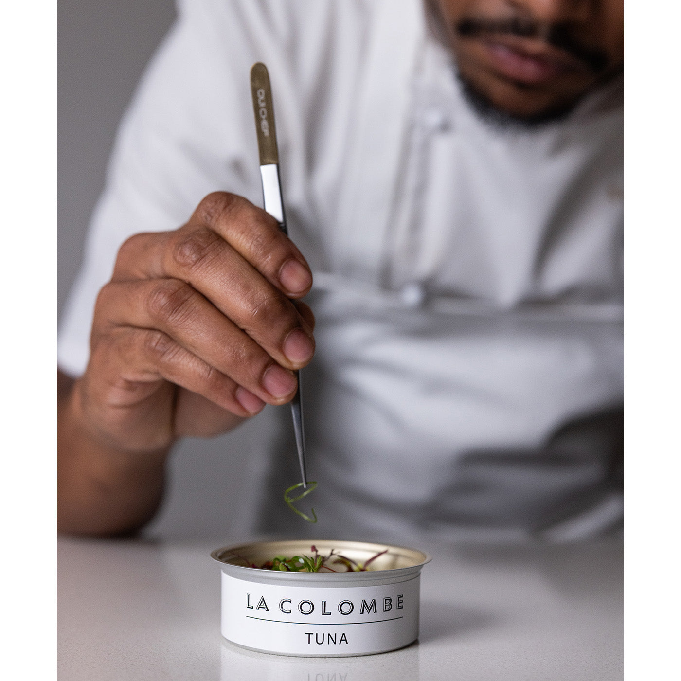 Person using Oui Chef Tweezers to serve tuna from a can labeled 'La Colombe Tuna'.