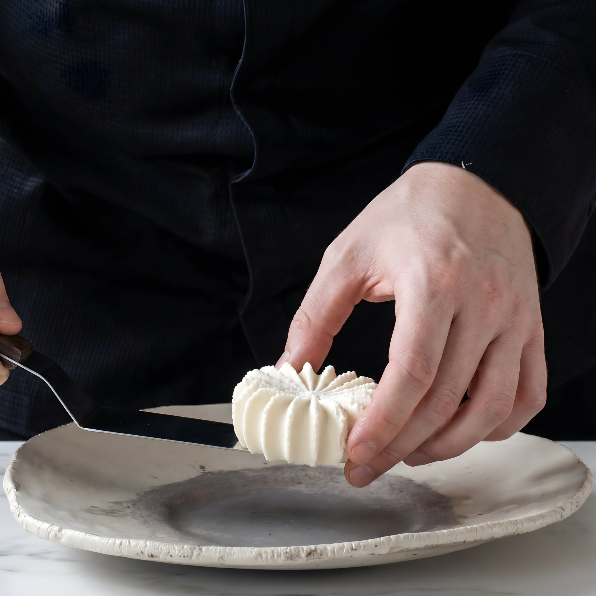 Chef elegantly placing a dessert onto a fine dining plate using a large stainless steel palette knife.